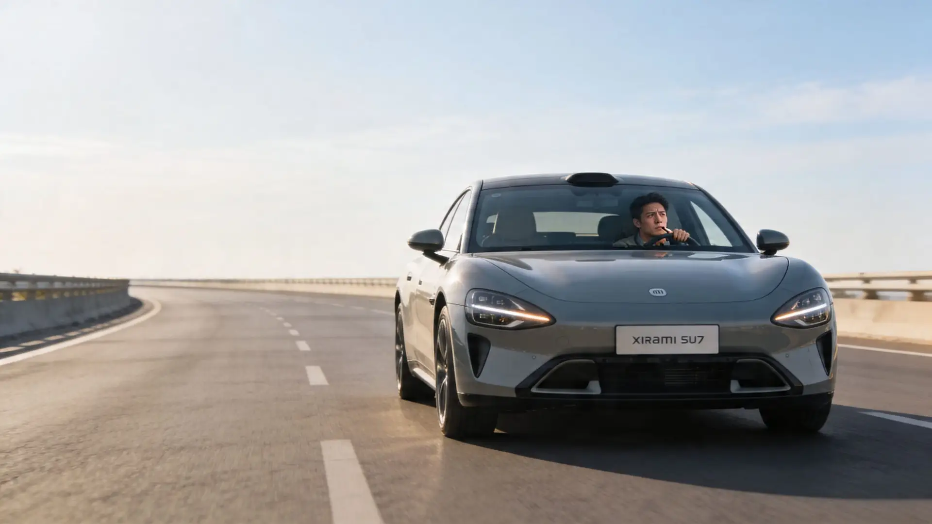 A gray Xiaomi SU7 electric sports car driving on an empty highway with a male driver.