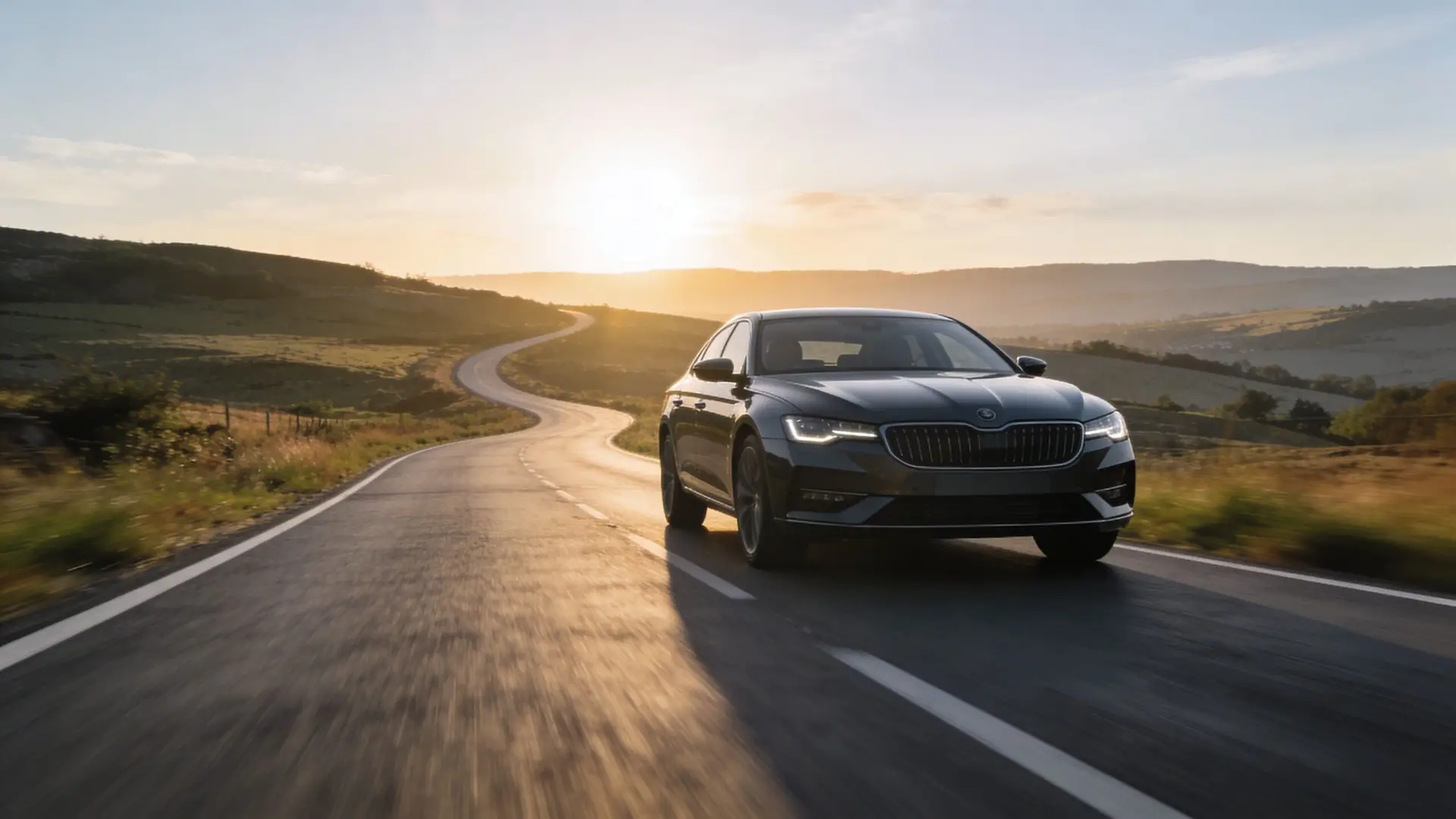 A modern dark sedan driving on a scenic road through rolling hills during a beautiful sunset.