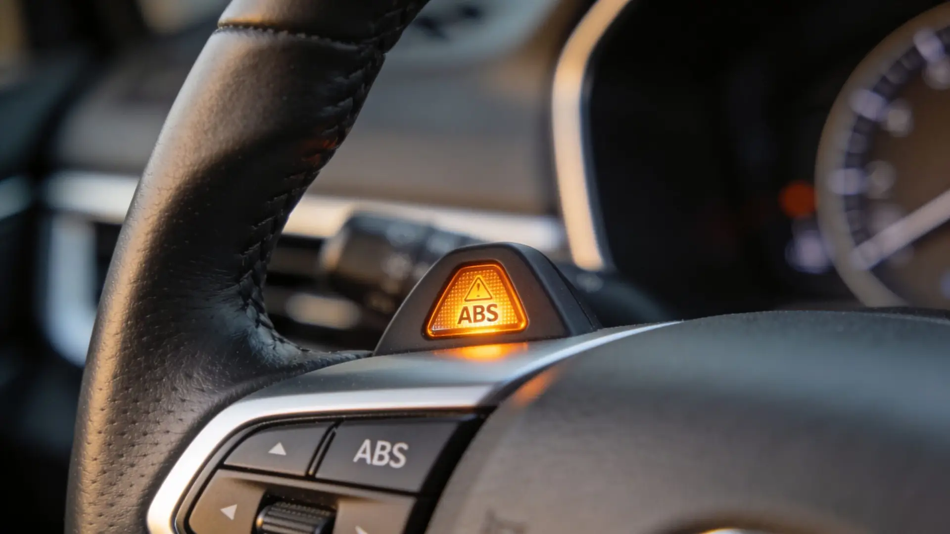 A close-up view of a car steering wheel with an illuminated ABS warning light indicator button.