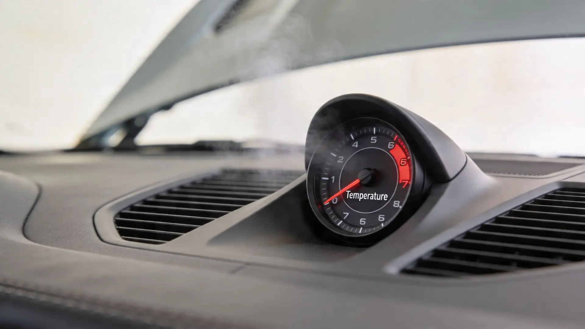 A close-up of a car dashboard showing a temperature gauge with steam rising from the vehicle interior.