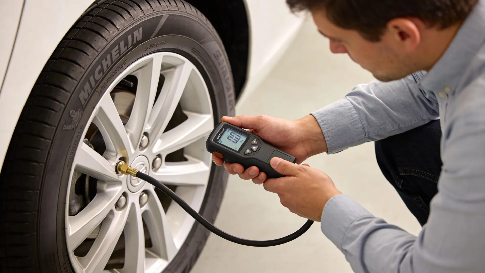 A man checking car tire pressure using a digital pressure gauge in a professional garage setting.