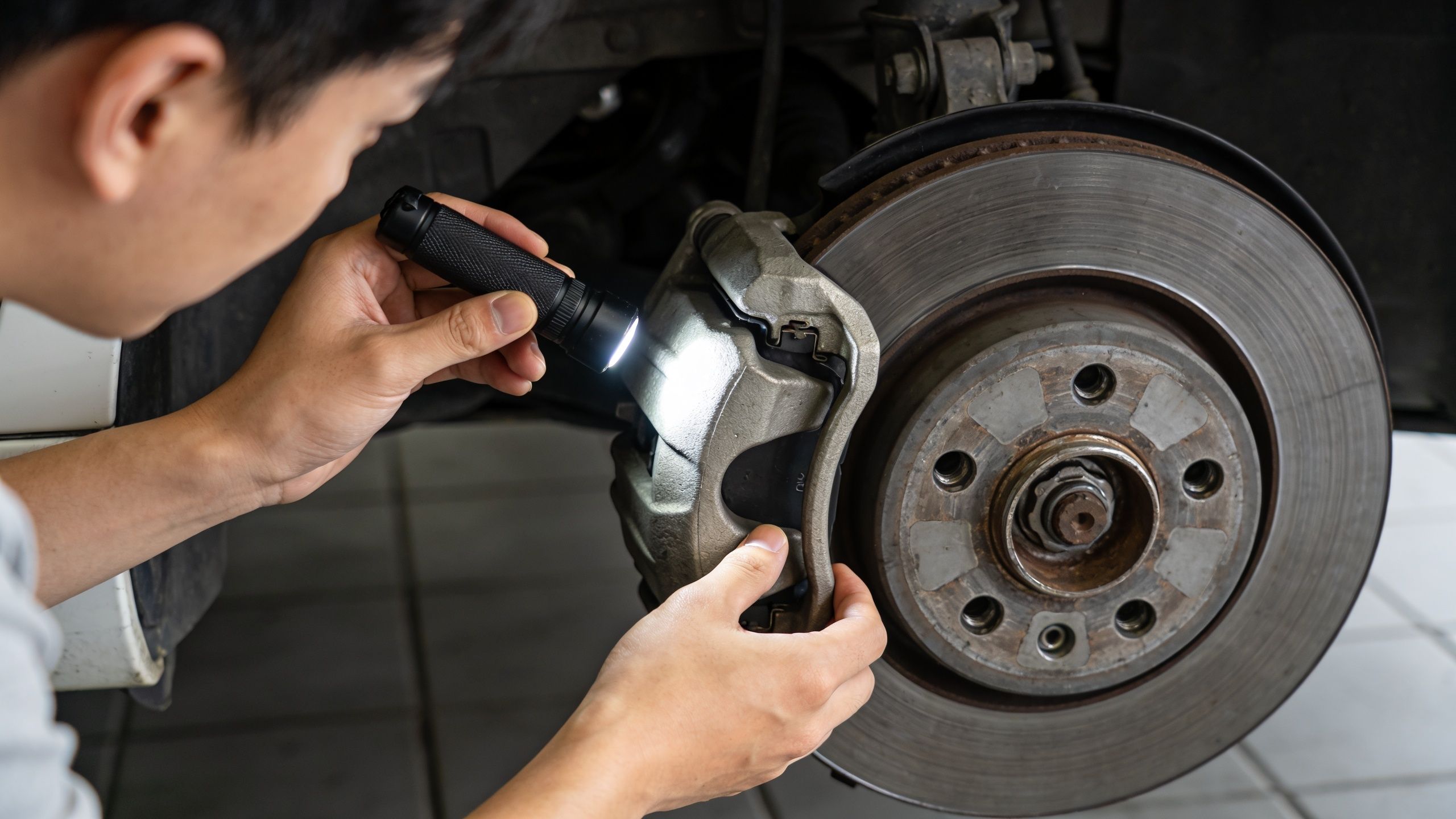 A professional mechanic inspecting a car's brake system using a flashlight to check for bad brake pads.